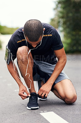 Buy stock photo Shot of a sporty young man tying his laces while out for a run