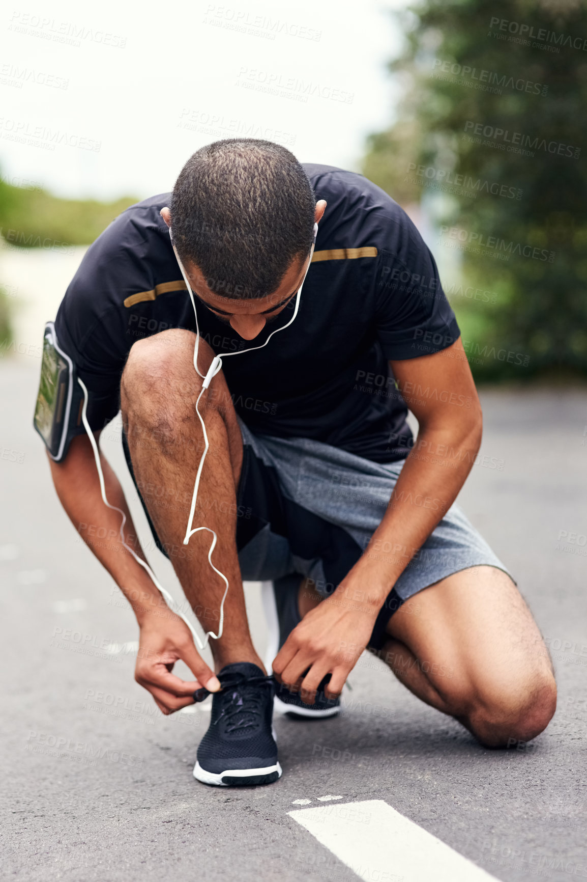 Buy stock photo Shot of a sporty young man tying his laces while out for a run