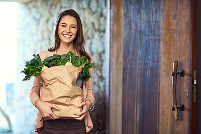 Buy stock photo Portrait of an attractive young woman arriving home with a bag full of groceries