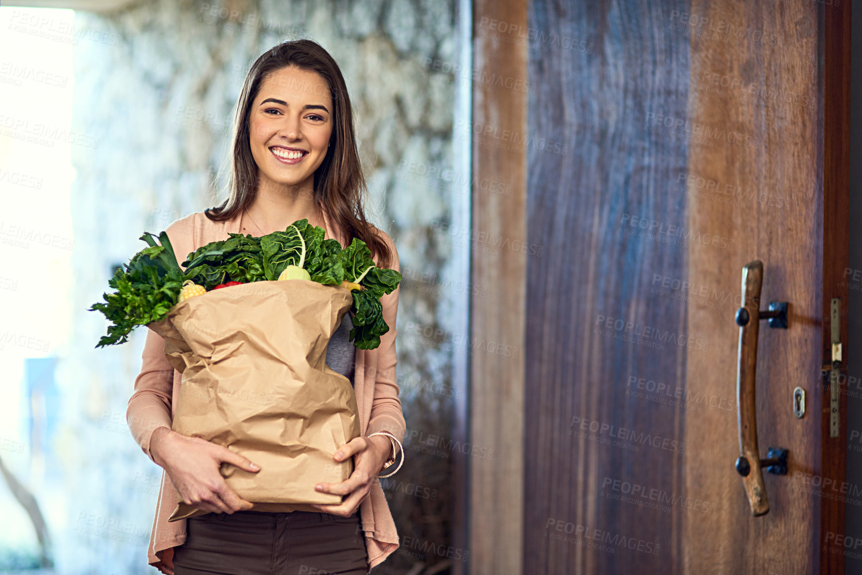 Buy stock photo Portrait of an attractive young woman arriving home with a bag full of groceries