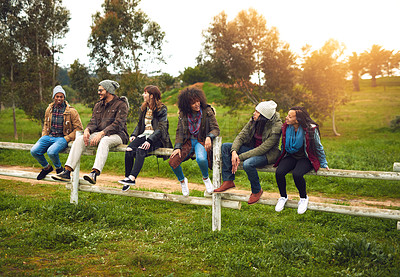 Buy stock photo Shot of a happy group of friends sitting in a row on a fence together