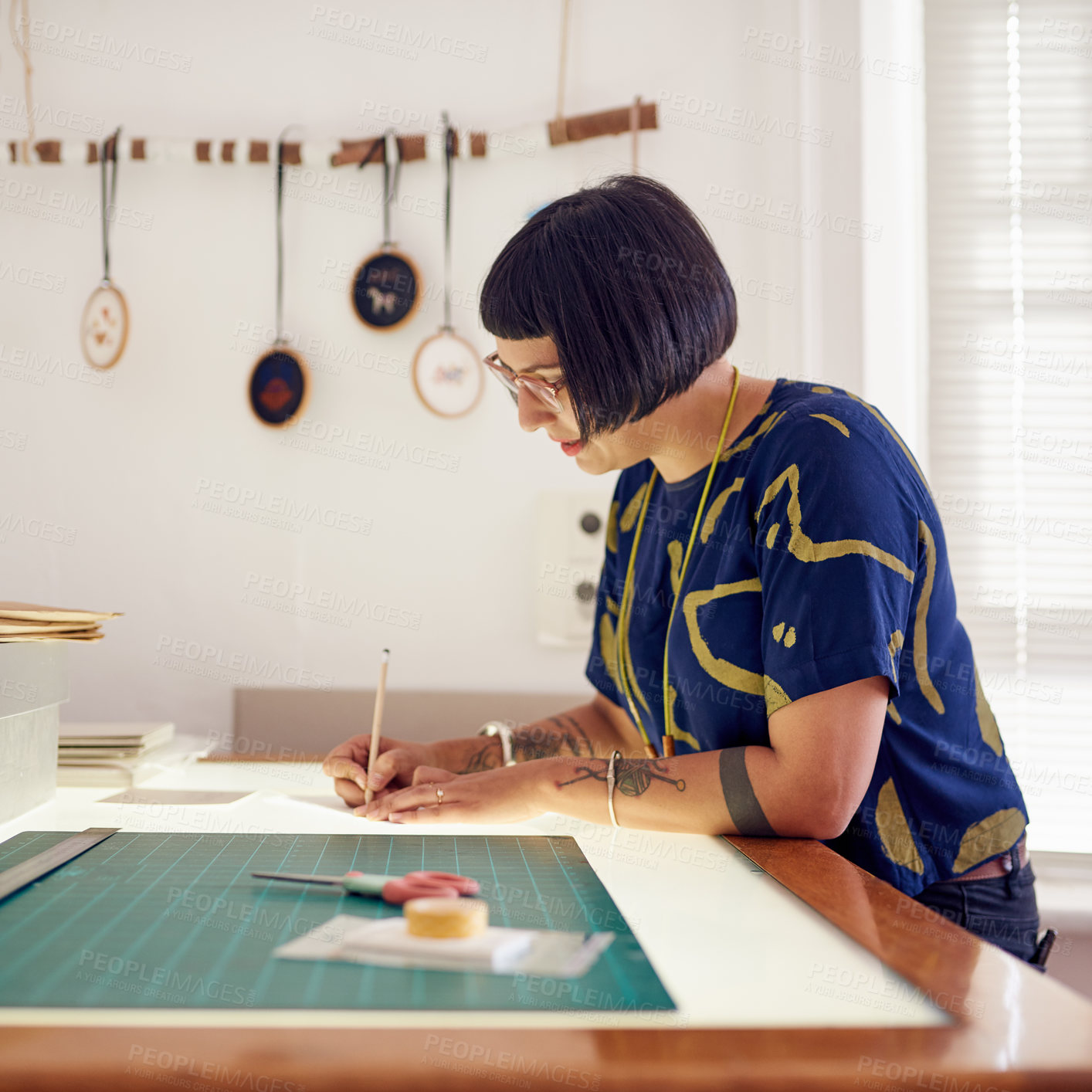 Buy stock photo Woman, table and designer drawing in studio, working and creative professional with cutting mat for measurements. Craftswoman, embroidery hoop and employee, planning and tracing pattern for crafts
