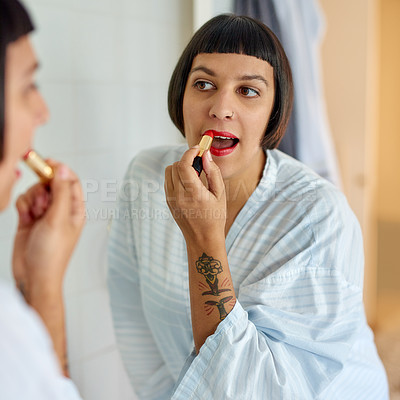 Buy stock photo Shot of a young woman in a bathrobe applying red lipstick in her bathroom mirror in the morning