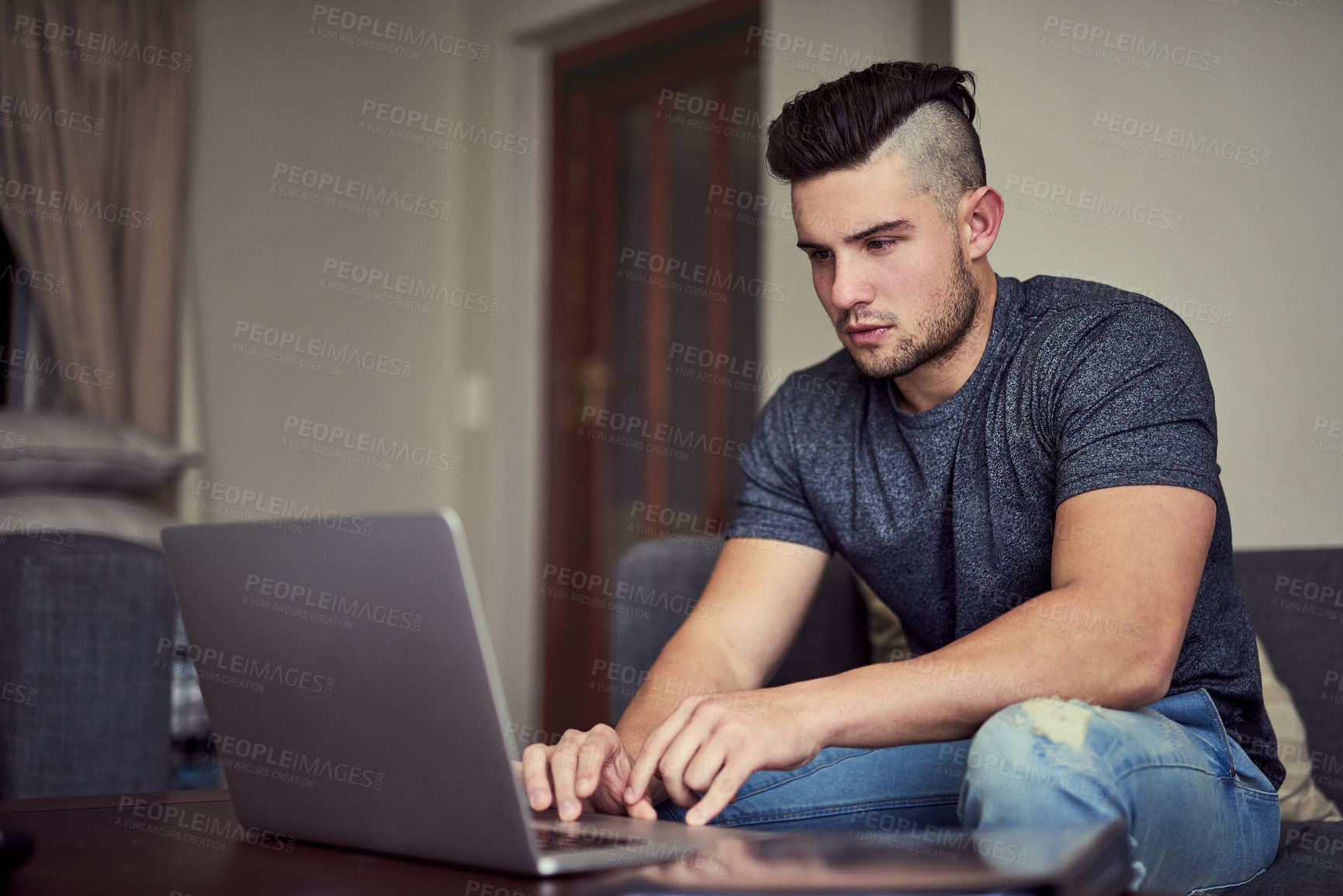 Buy stock photo Shot of a driven young man using his laptop to work from home