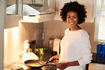 Buy stock photo Shot of a happy young woman cooking a fried egg at home