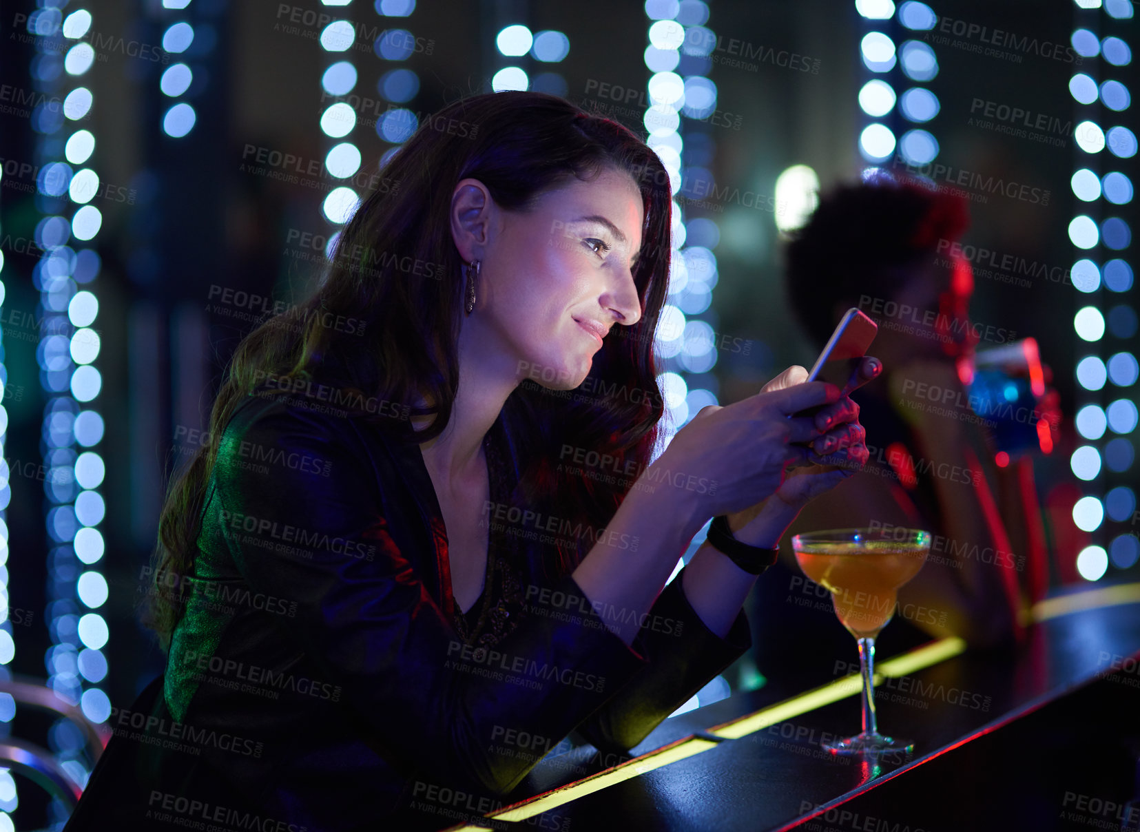 Buy stock photo Shot of a smiling young woman reading a text message while sitting at the bar in a nightclub