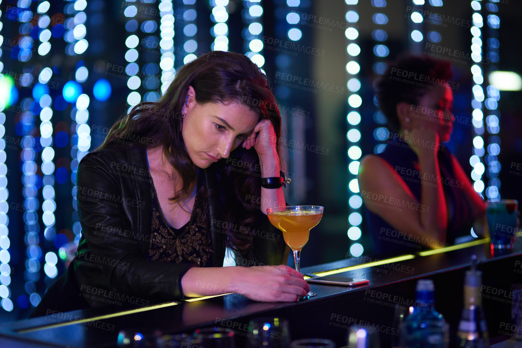 Buy stock photo Shot of a depressed young woman drinking a cocktail at the bar in a nightclub