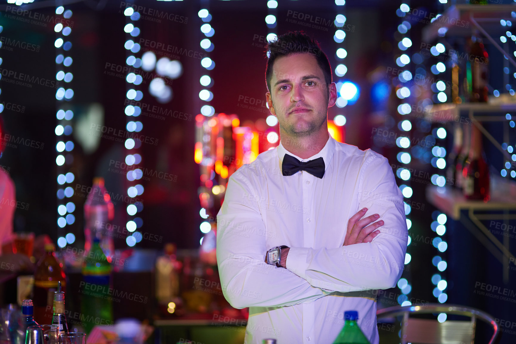 Buy stock photo Portrait of a serious looking bartender standing with his arms crossed in a nightclub