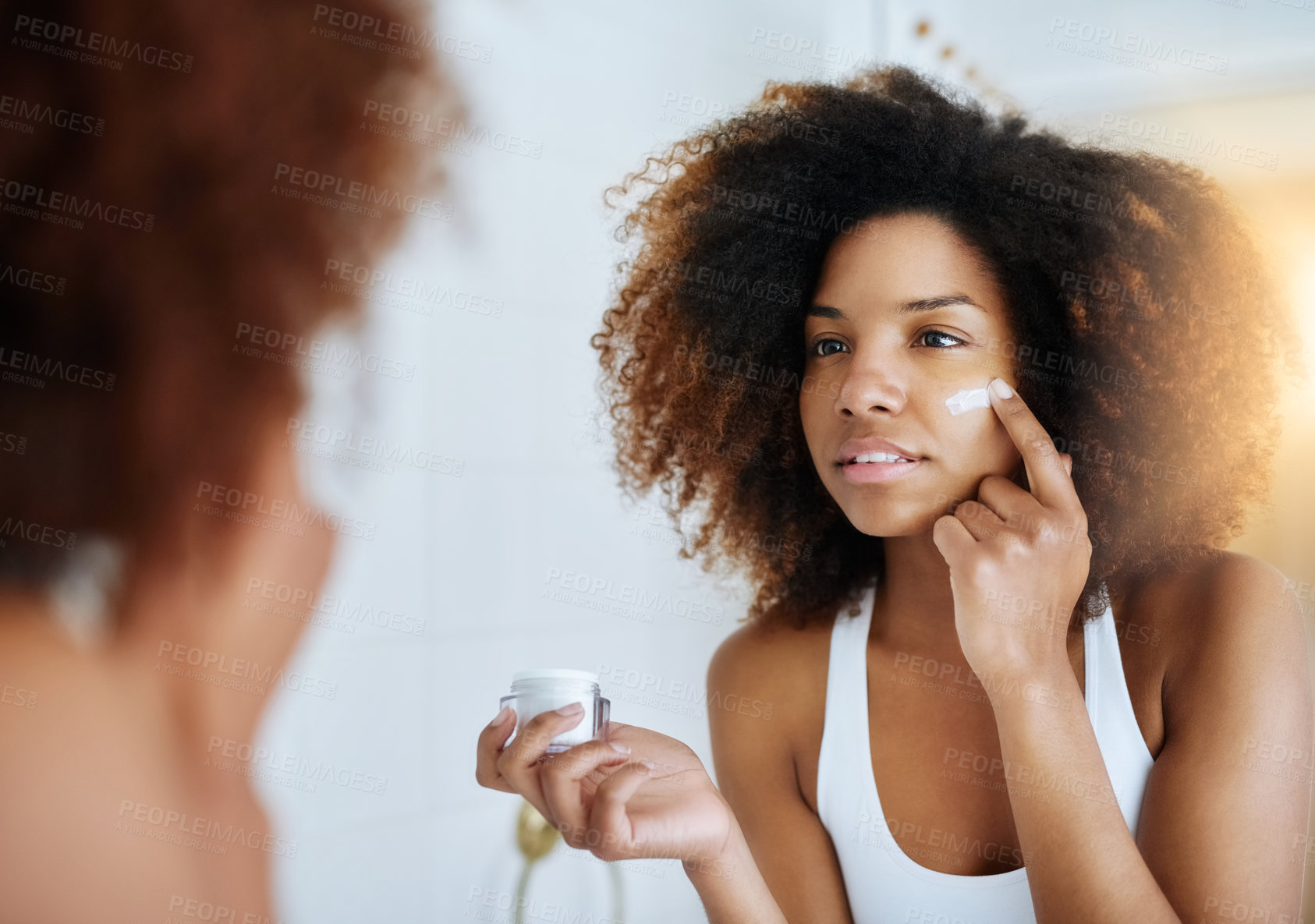 Buy stock photo Shot of an attractive young woman applying moisturizer to her face in front of the mirror