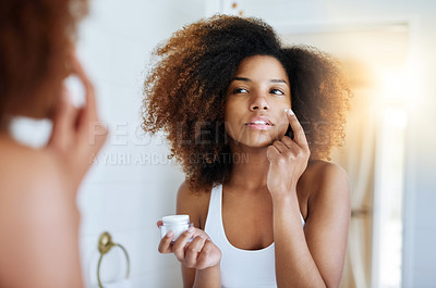 Buy stock photo Shot of an attractive young woman applying moisturizer to her face in front of the mirror