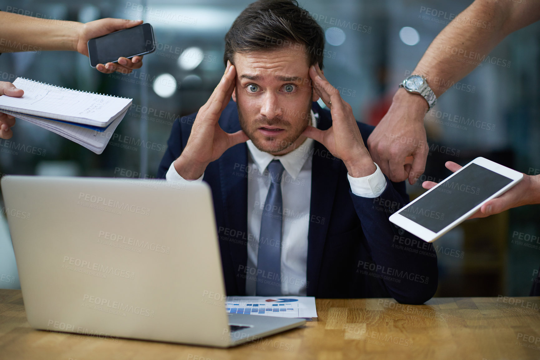 Buy stock photo Portrait of a stressed out looking businessman surrounded by demanding colleagues while sitting at a desk in an office