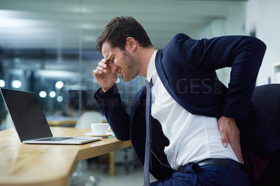 Buy stock photo Shot of a businessman wincing in pain and holding his lower back while sitting at a desk in an office