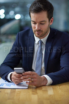 Buy stock photo Shot of a businessman using a cellphone while sitting at a desk in an office
