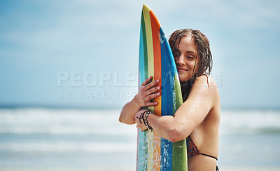 Buy stock photo Shot of an attractive young woman standing on a beach hugging her surfboard