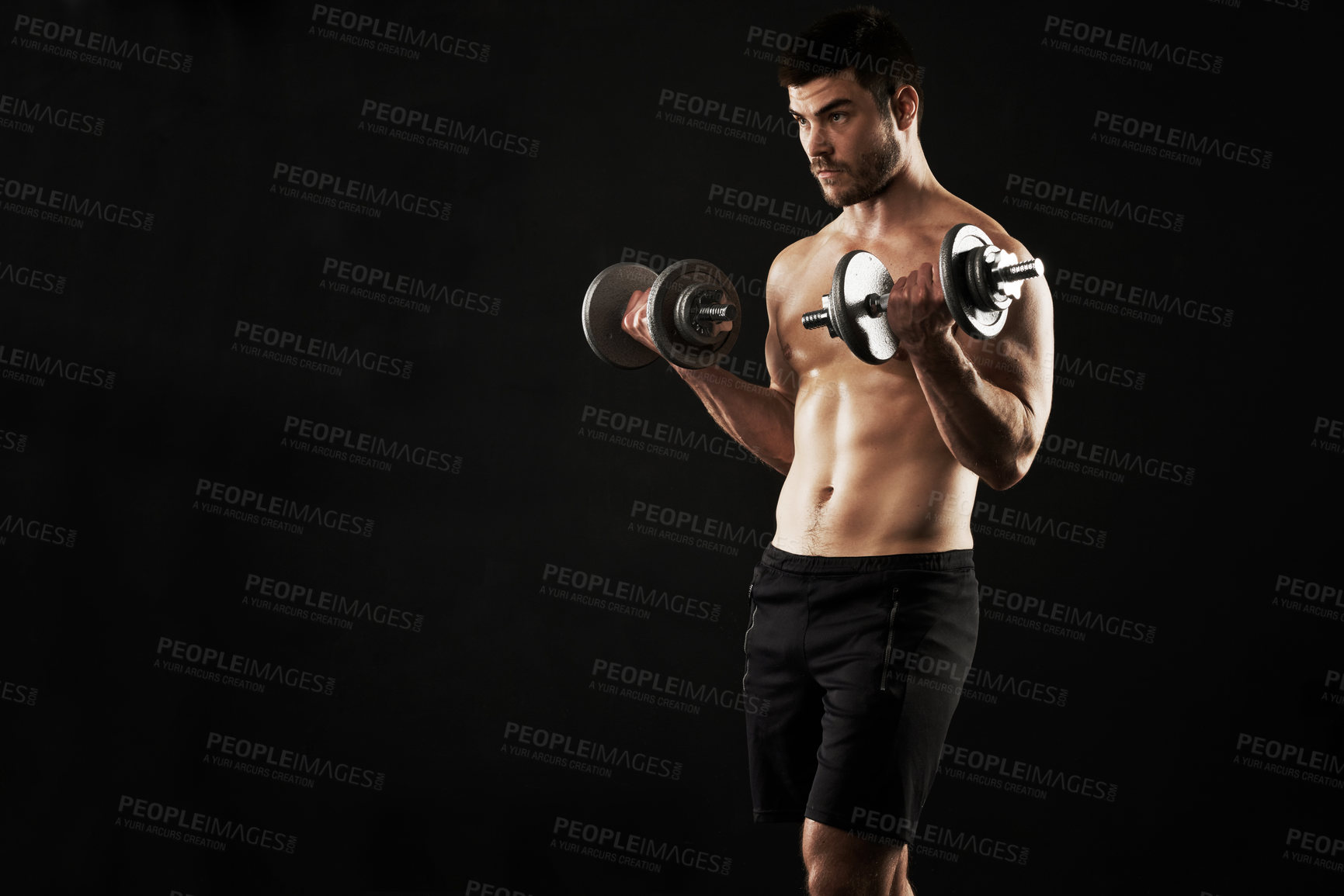 Buy stock photo Studio shot of a sporty young man working out with dumbbells isolated on black