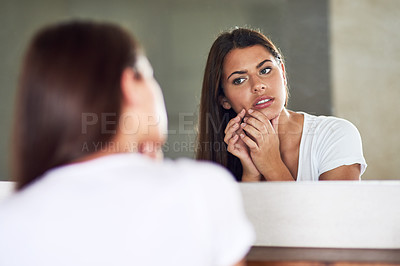 Buy stock photo Shot of a frowning young woman examining an imperfection on her skin in the mirror at home