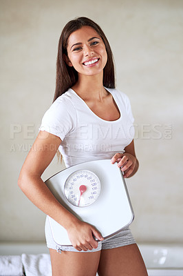 Buy stock photo Portrait of a happy young woman holding her scale while standing in the bathroom