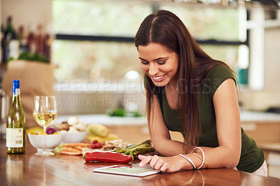 Buy stock photo Shot of an attractive young woman using her tablet to look up a recipe in her kitchen