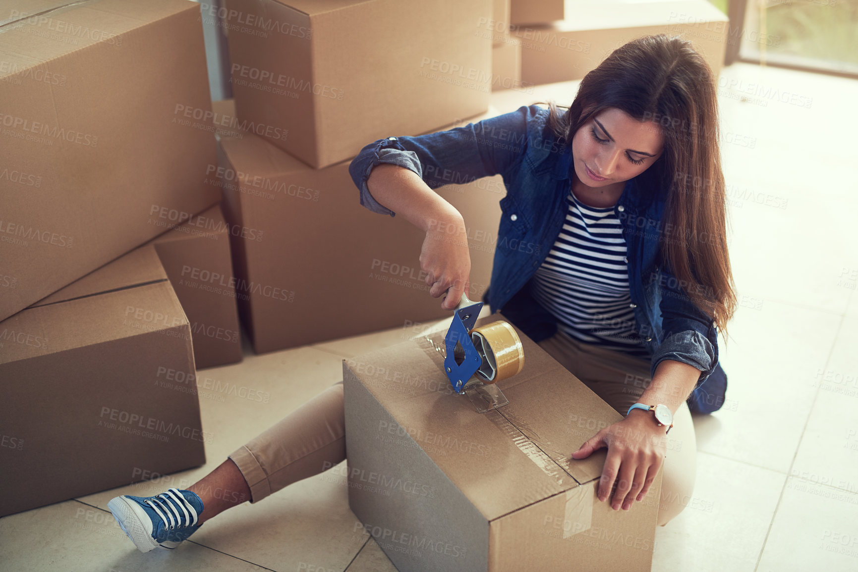 Buy stock photo Shot of a young woman packing boxes while moving house