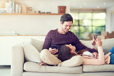 Buy stock photo Shot of a smiling young couple using digital tablets while relaxing together on the sofa at home