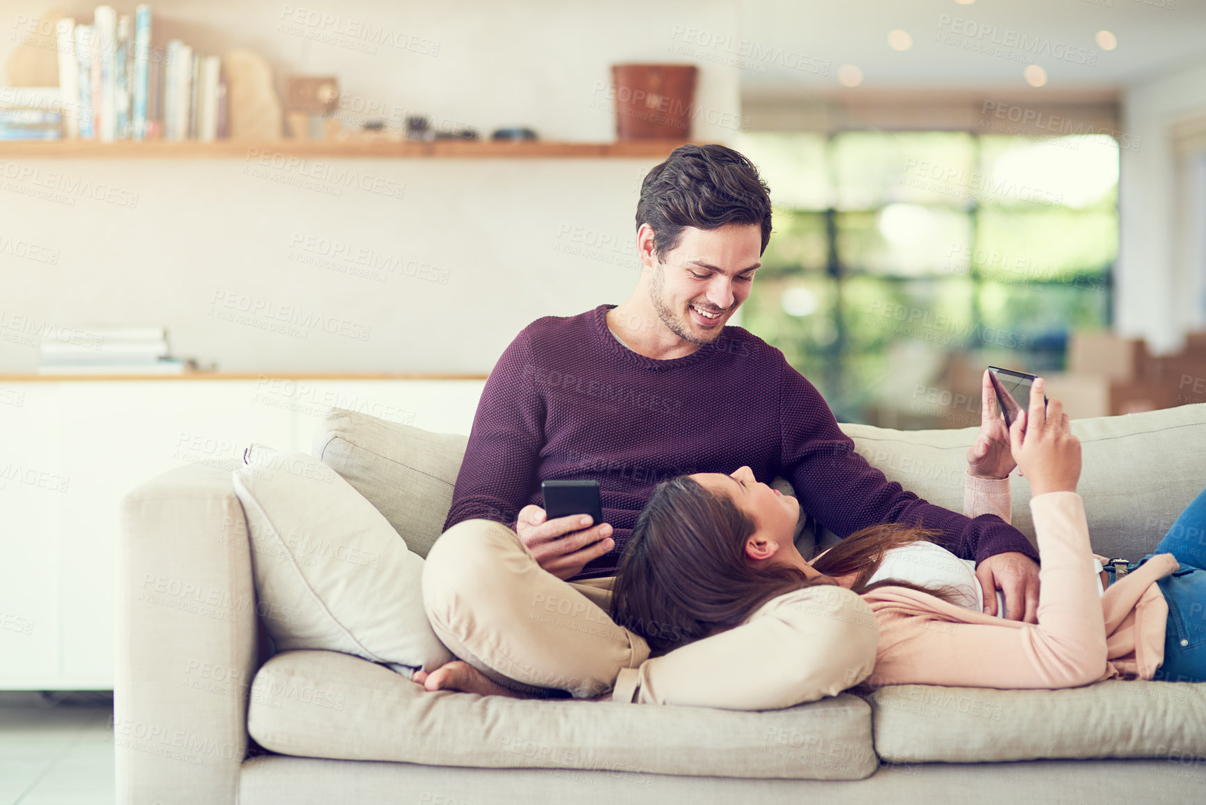 Buy stock photo Tablet, phone and couple relaxing in living room for entertainment together on sofa at home. Happy, love and people online networking on cellphone and digital technology in lounge at apartment.