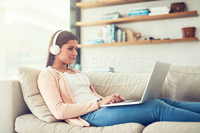 Buy stock photo Shot of a young woman listening to music on a laptop while relaxing on the sofa at home