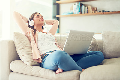 Buy stock photo Shot of a young woman listening to music on a laptop while relaxing on the sofa at home