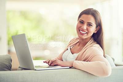 Buy stock photo Portrait of a smiling young woman using a laptop while relaxing on the sofa at home