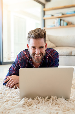 Buy stock photo Shot of a relaxed young man using a laptop on the floor at home