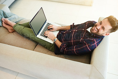 Buy stock photo Shot of a relaxed young man using a laptop on the sofa at home