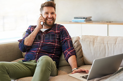 Buy stock photo Shot of a young man using a laptop and mobile phone on the sofa at home