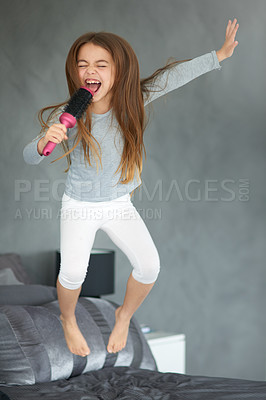 Buy stock photo Shot of a cute little girl jumping on a bed while pretending to sing into a hairbrush