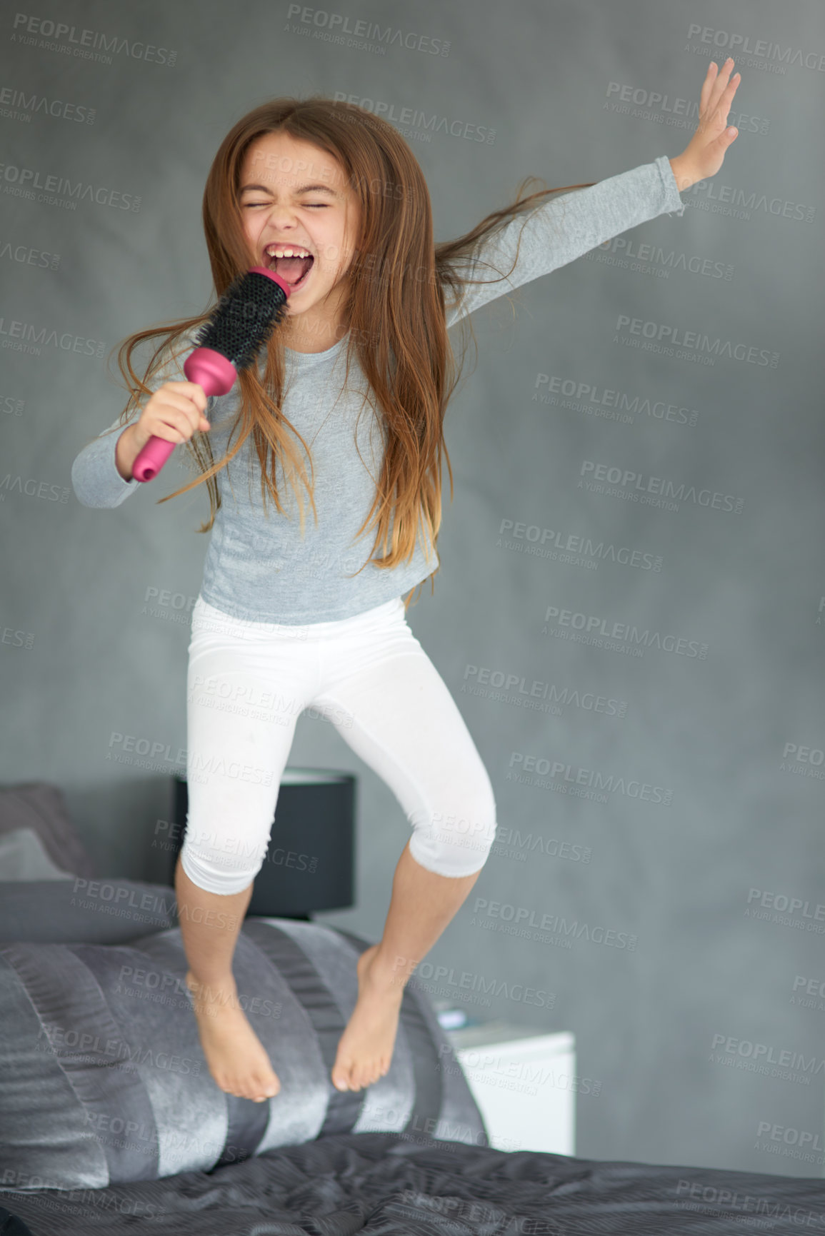 Buy stock photo Shot of a cute little girl jumping on a bed while pretending to sing into a hairbrush