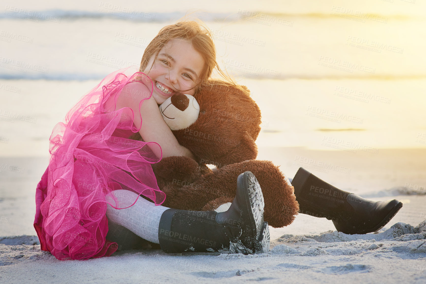Buy stock photo Girl, hug and teddy bear on beach with portrait for happiness, excitement and fun by ocean at sunset. Female child, stuffed animal and boots in sand for love, pleasure and outing in nature with toys