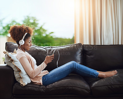 Buy stock photo Shot of a young woman relaxing on the sofa and listening to music on her phone