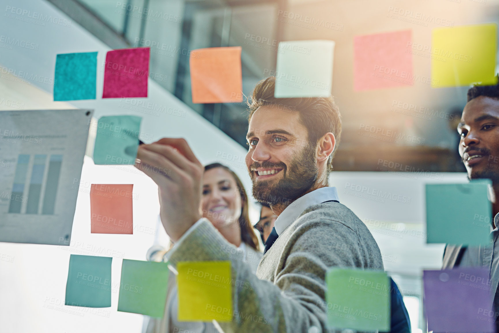 Buy stock photo Cropped shot of a group of businesspeople brainstorming with sticky notes on a glass wall in an office