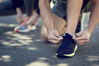 Buy stock photo Cropped shot of two unrecognizable people tying their laces before a run