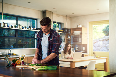 Buy stock photo Cropped shot of a young man preparing a meal with his girlfriend in the background at home