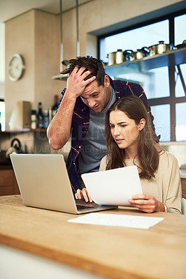 Buy stock photo Cropped shot of a young couple looking anxious while using a laptop and going through paperwork together at home