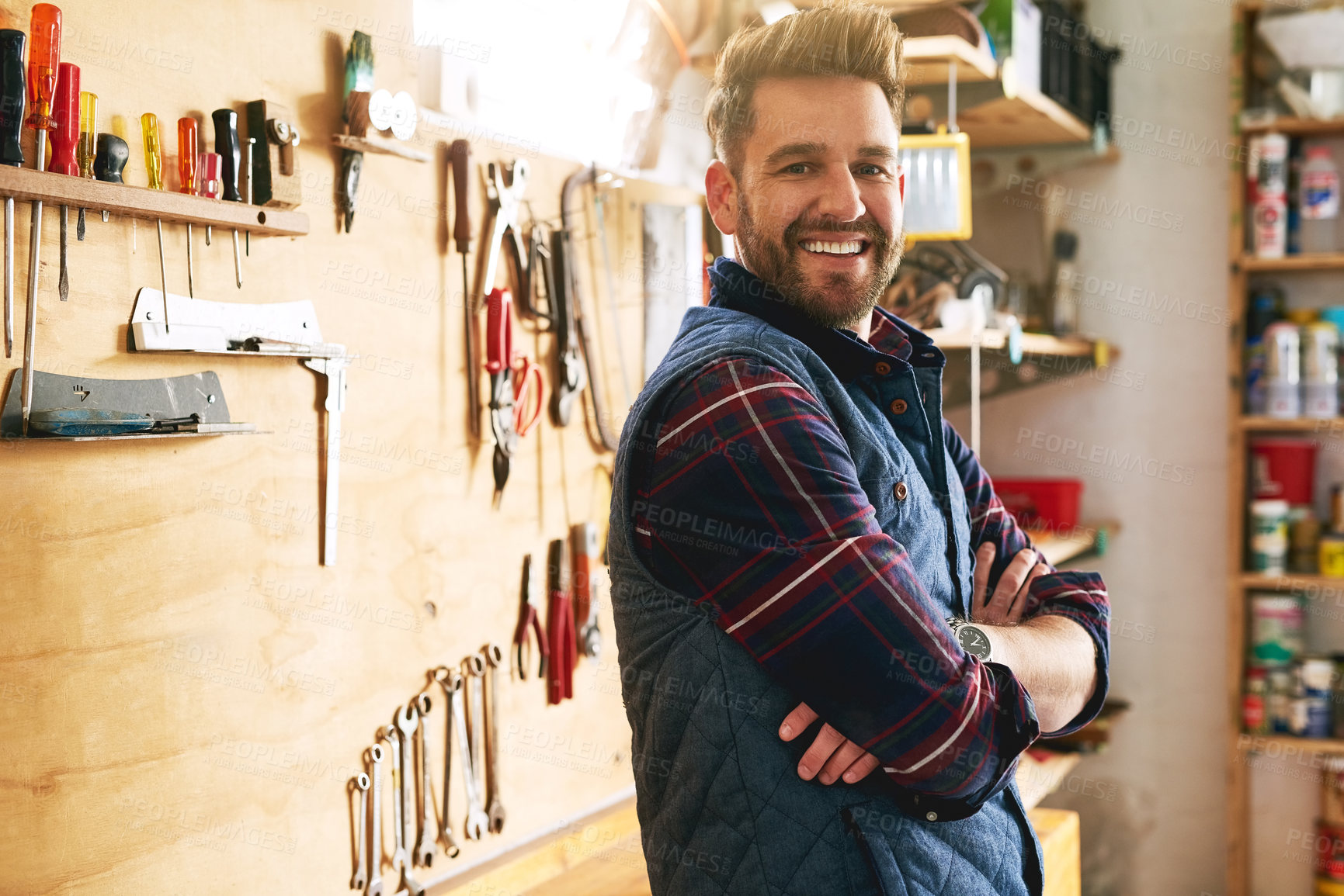 Buy stock photo Portrait of a handsome young handyman standing with his arms folded in a workshop