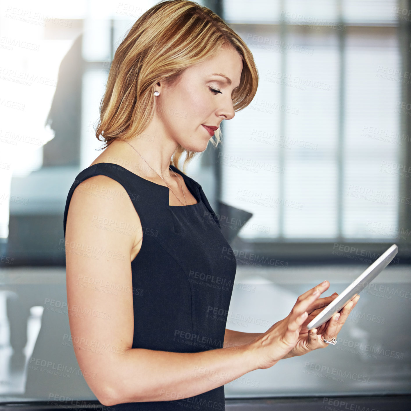 Buy stock photo Shot of a well dressed businesswoman using a tablet while standing in the office