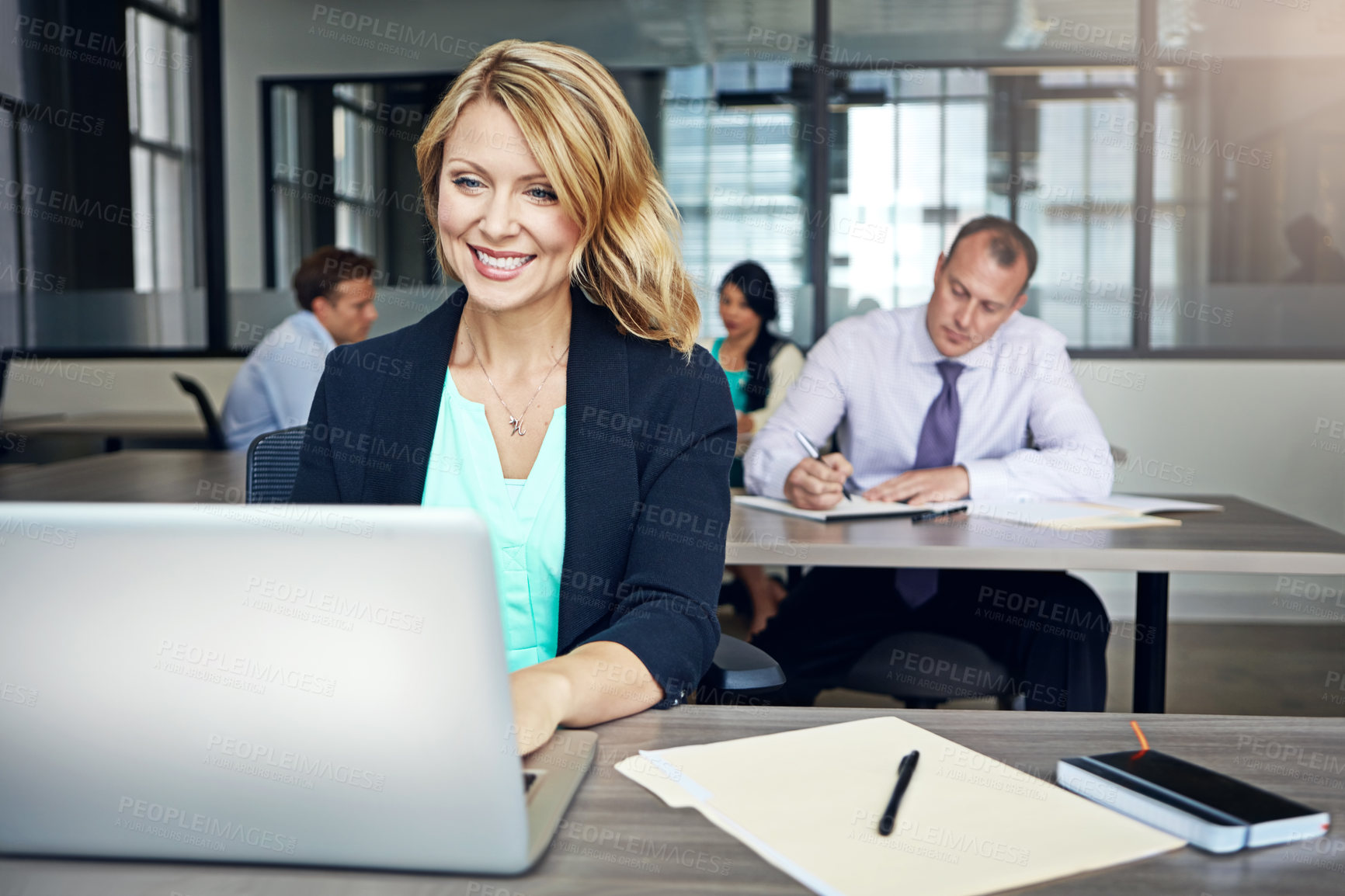 Buy stock photo Shot of a businesswoman using a laptop at her desk with her colleagues in the background