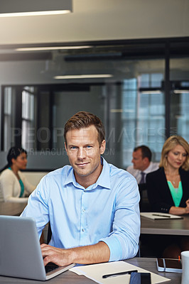 Buy stock photo Portrait of a businessman using a laptop at his desk with his colleagues in the background