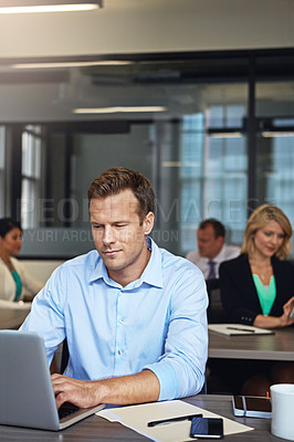 Buy stock photo Shot of a businessman using a laptop at his desk with his colleagues in the background