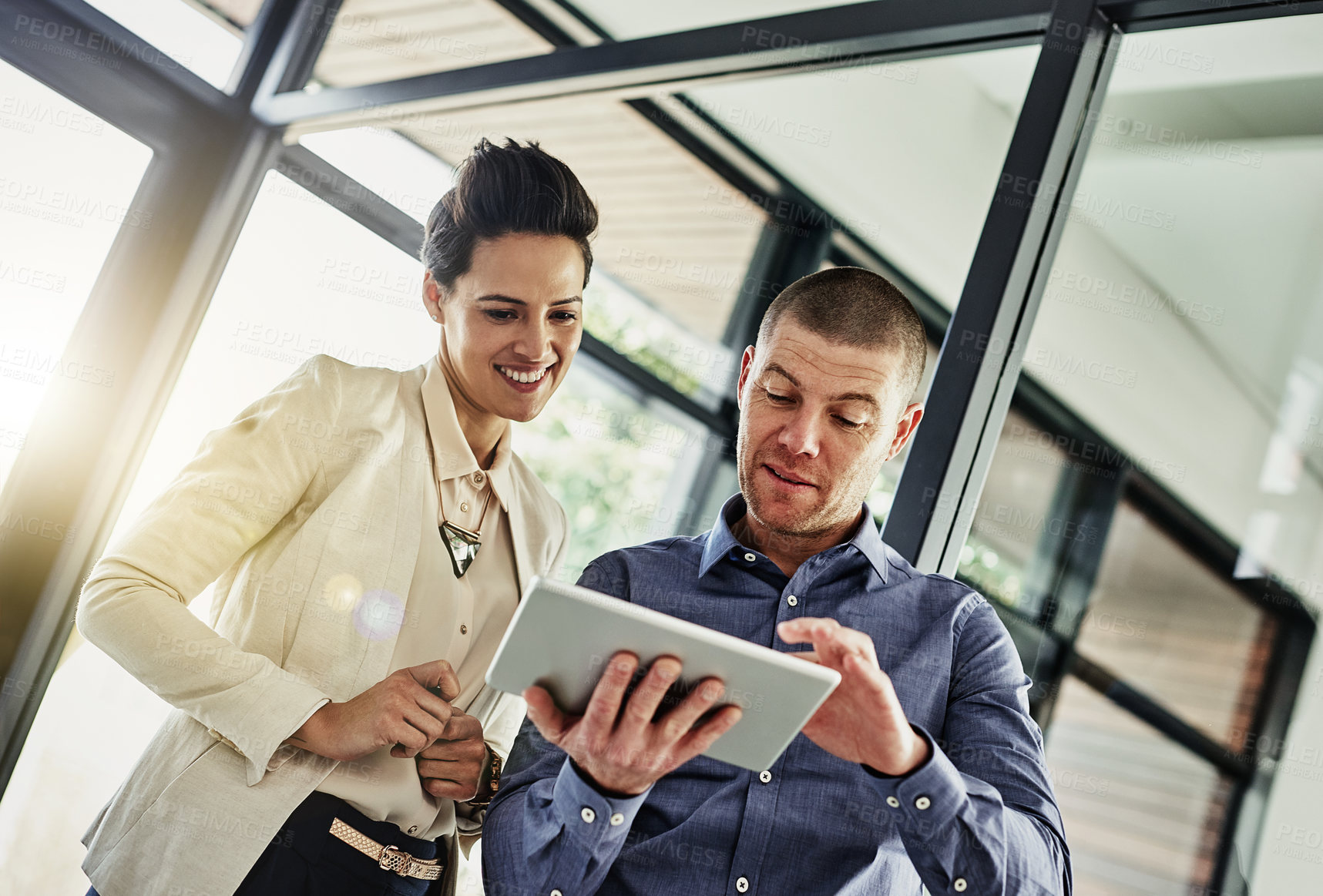 Buy stock photo Shot of two colleagues using a tablet while meeting in their office