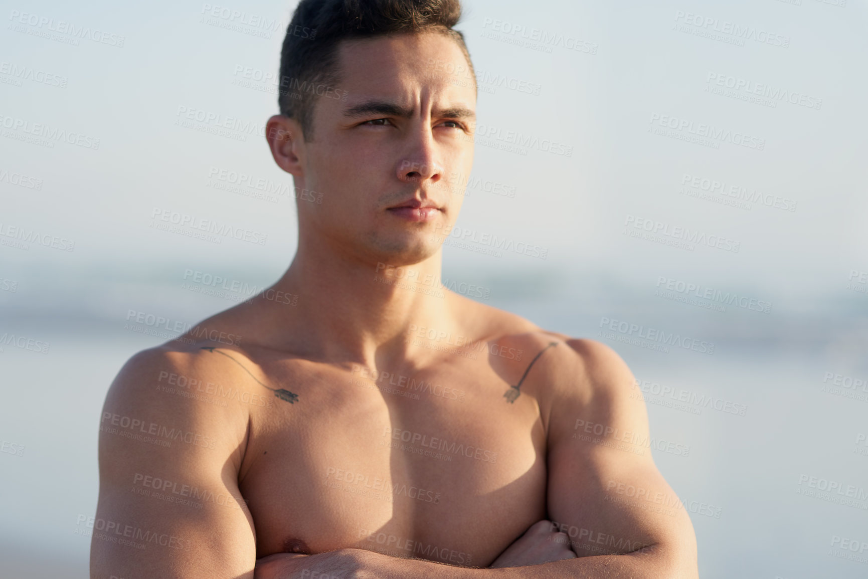 Buy stock photo Cropped shot of a handsome young man standing with his arms folded at the beach