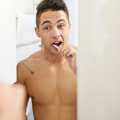 Buy stock photo Shot of a handsome young man brushing his teeth in his bathroom