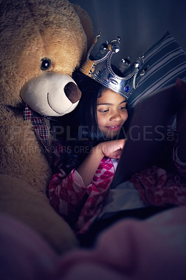 Buy stock photo Cropped shot of a little girl using a digital tablet while lying in bed with her teddy at night