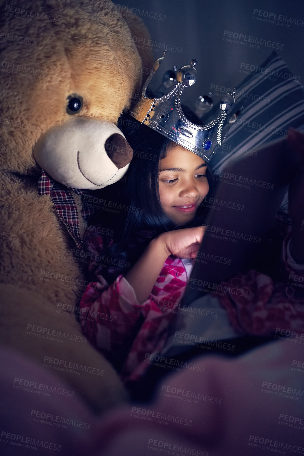 Buy stock photo Cropped shot of a little girl using a digital tablet while lying in bed with her teddy at night