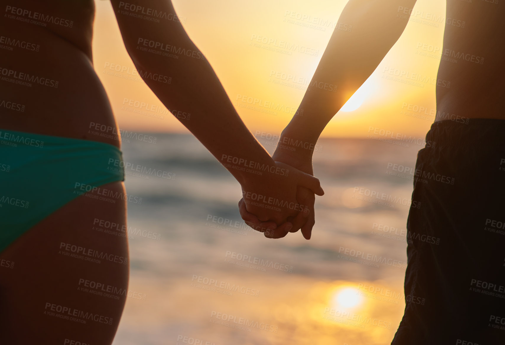 Buy stock photo Closeup shot of a young couple holding hands while watching the sunset at the beach